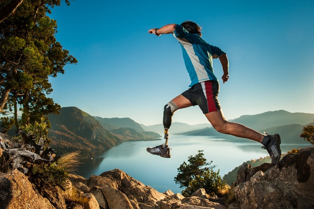 Runner with a prosthetic leg leaping over rocks above a mountain lake