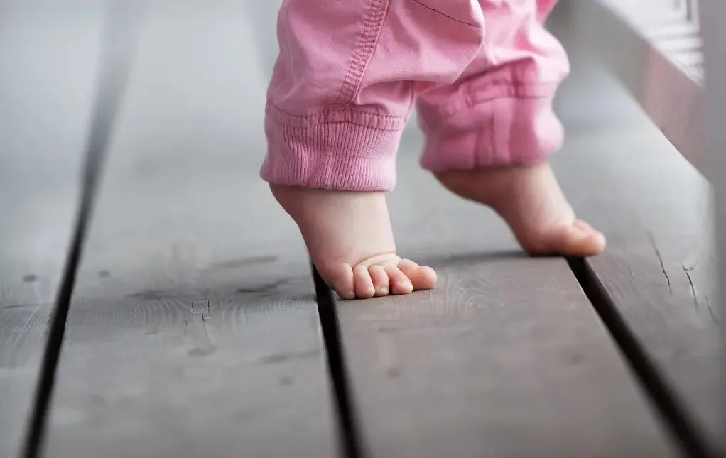 Toddler in pink pants walking on tiptoes on a wooden floor