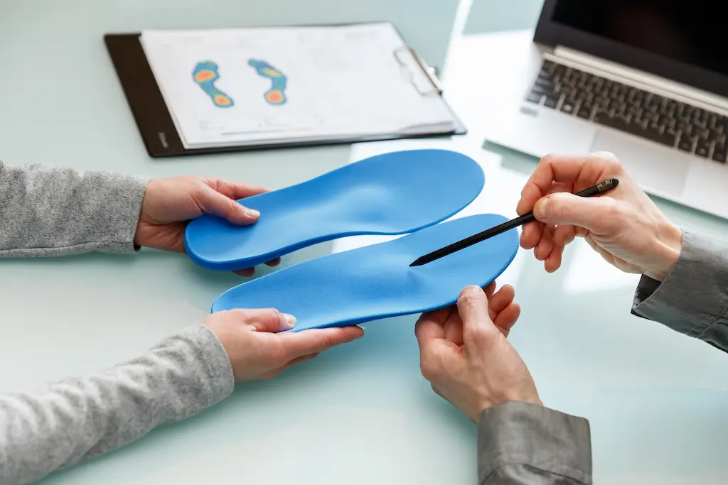 Specialist holding up a pair of blue custom orthotic insoles beside a foot scan