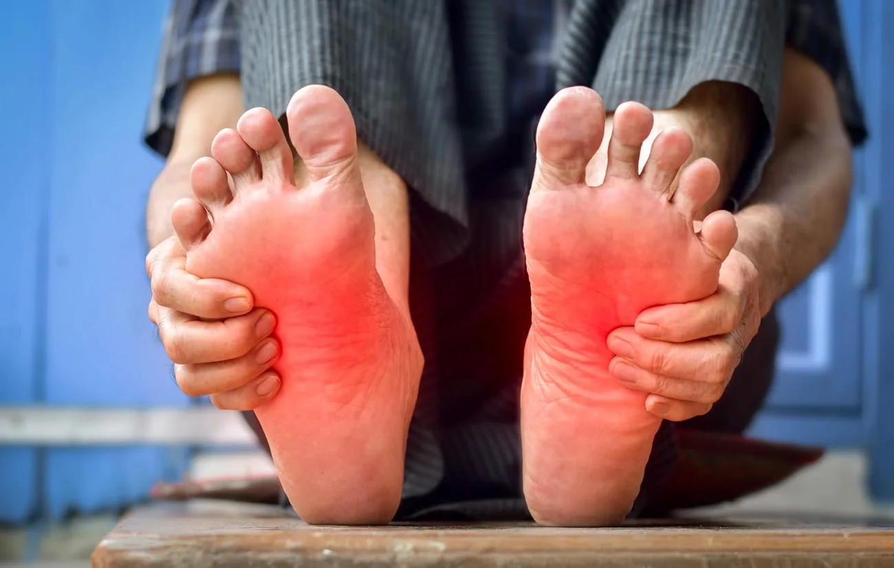 Person holding both feet with red areas marking foot pain