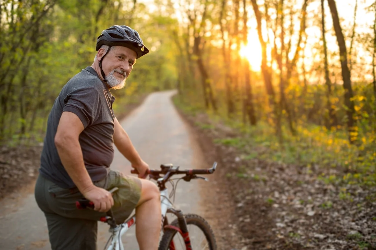 Older man in a helmet with a bicycle on a forest trail