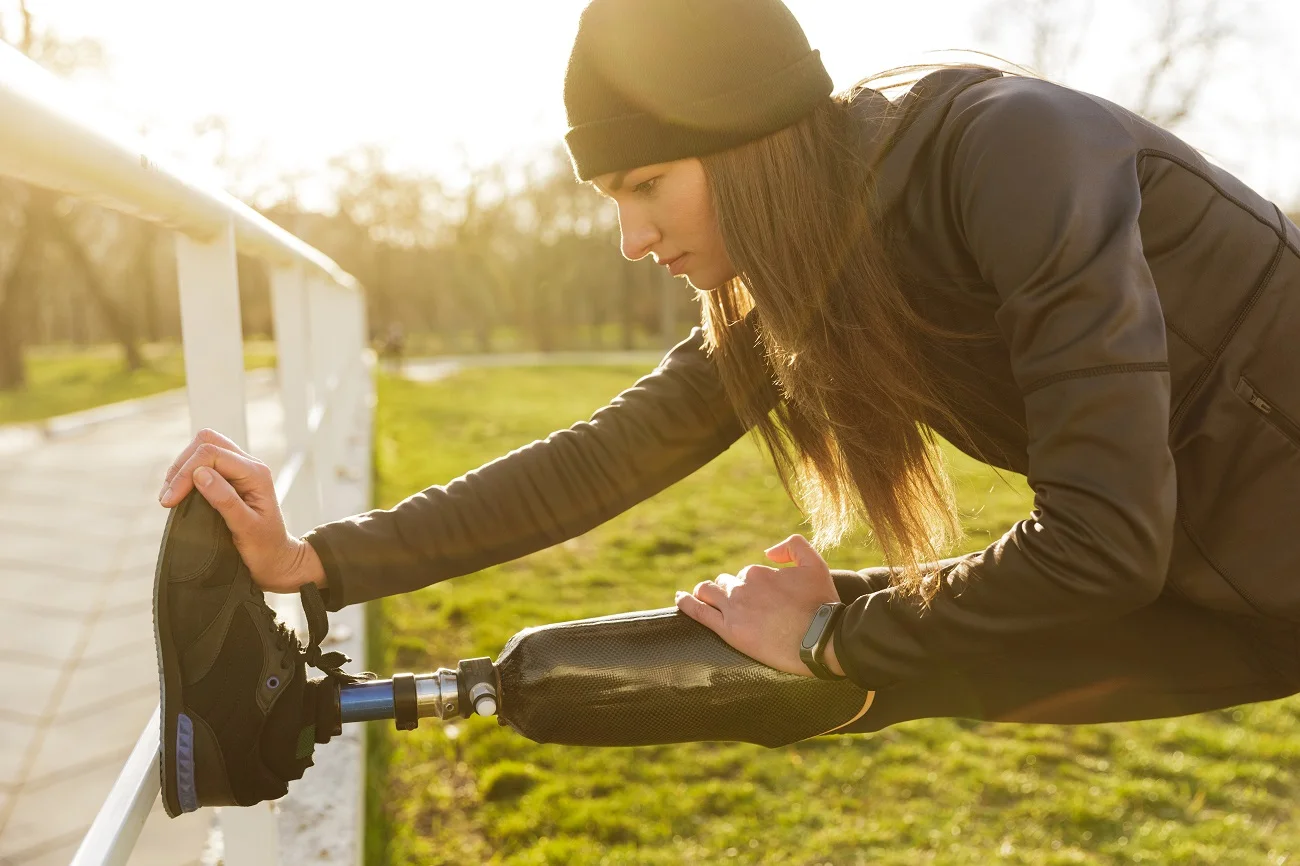 Woman with a prosthetic leg stretching against a fence outdoors