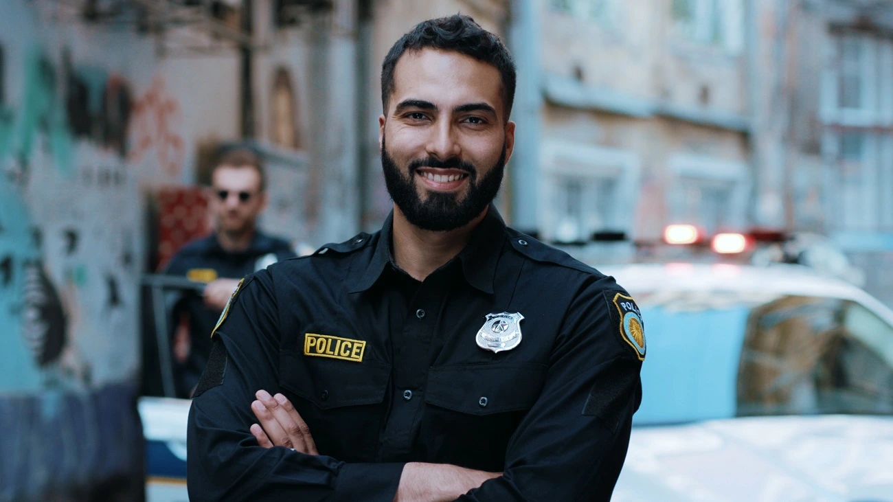 Smiling police officer in uniform standing in front of a patrol car