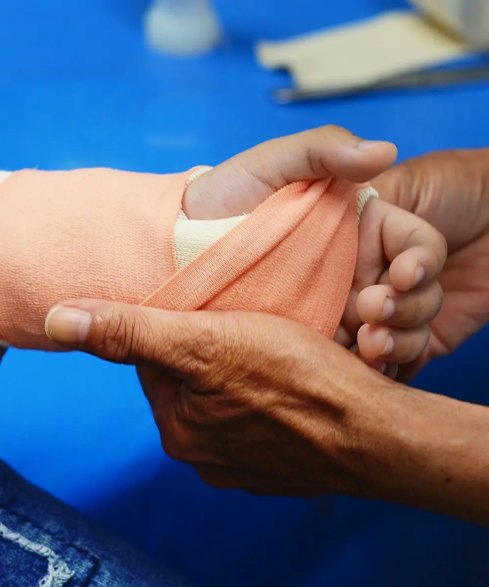 Manos envolviendo una venda alrededor de la mano y la muñeca de un paciente.