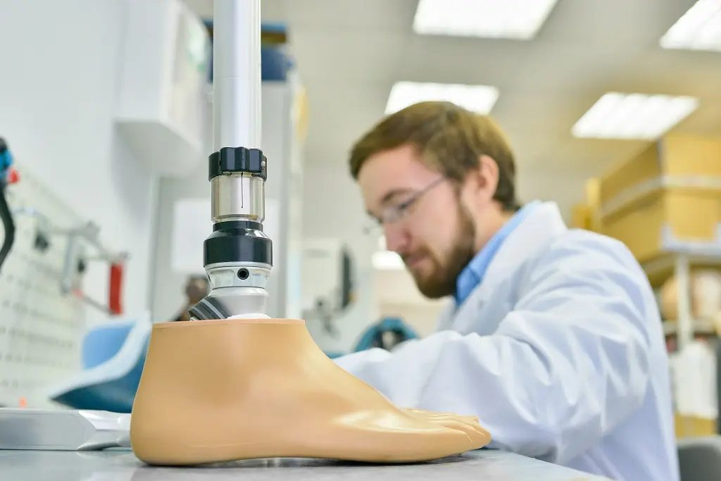 Técnico trabajando junto a un pie protésico sobre un pilón en un laboratorio.