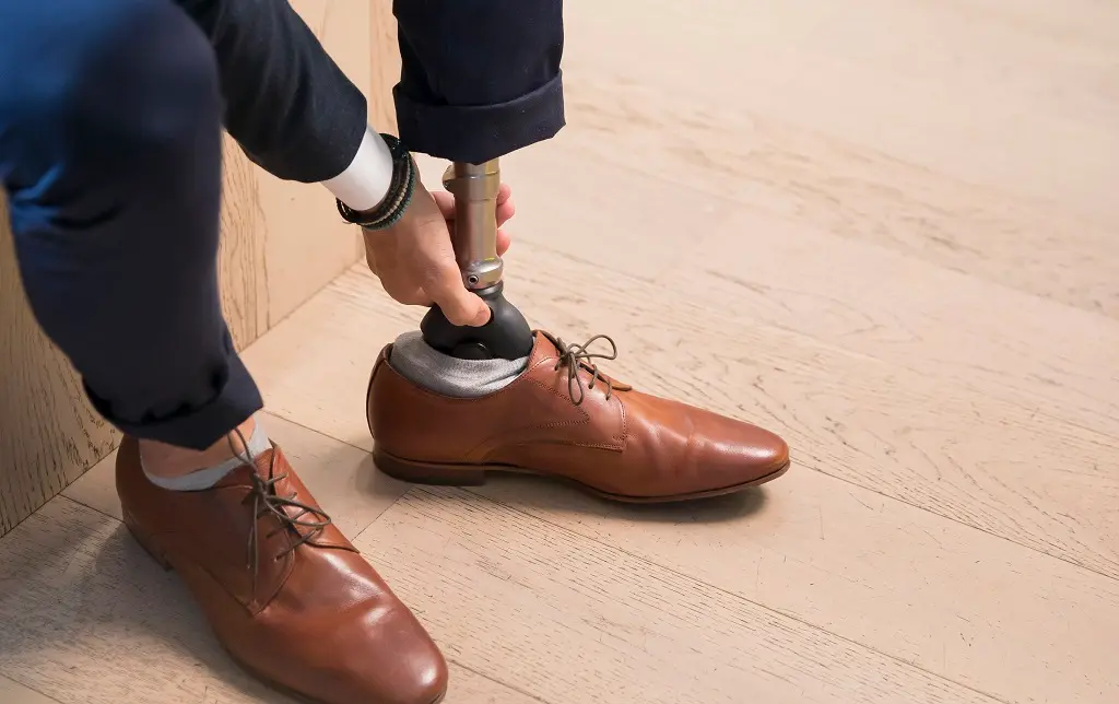 Hombre colocando su pierna protésica en un zapato de vestir marrón.