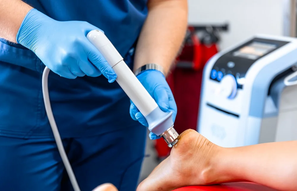 Médico tratando el talón de un paciente con un dispositivo de terapia de ondas de choque.