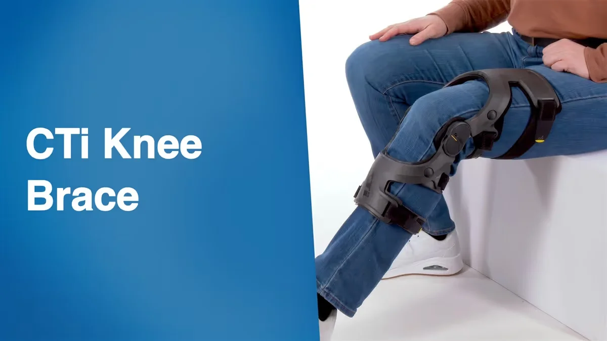 Person sitting wearing a black CTi knee brace on their left leg with blue jeans and white sneakers.