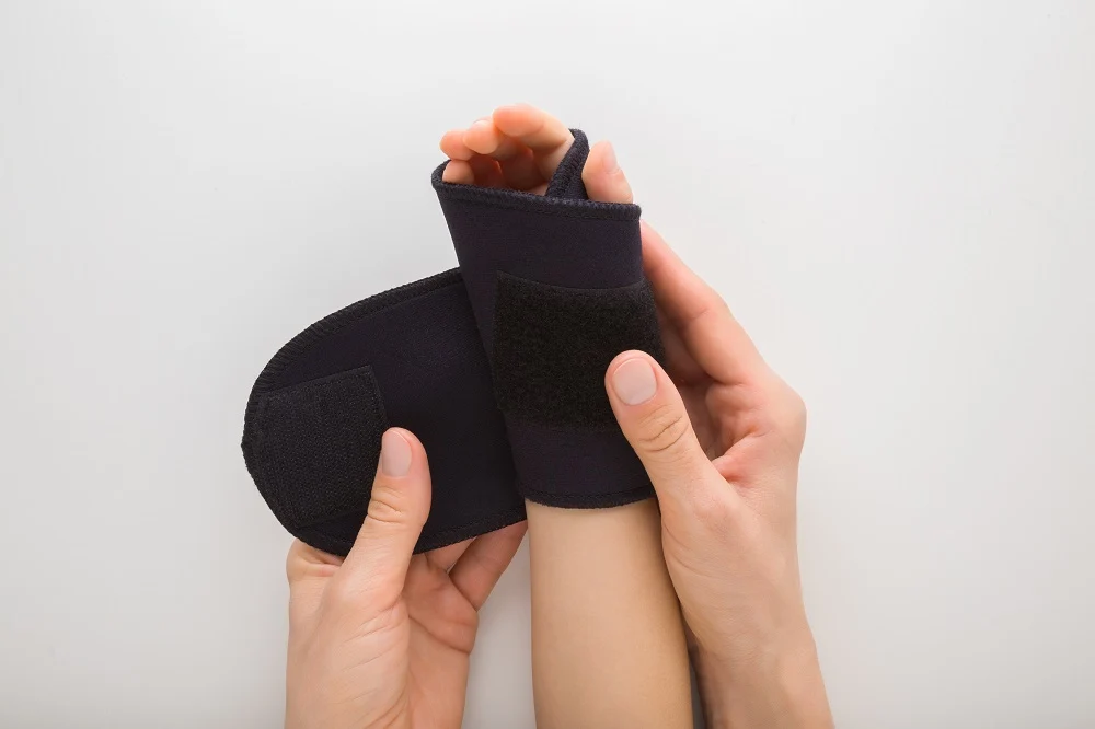 Manos de adulto ajustando una férula negra para la muñeca con un orificio para el pulgar en la muñeca de un niño.